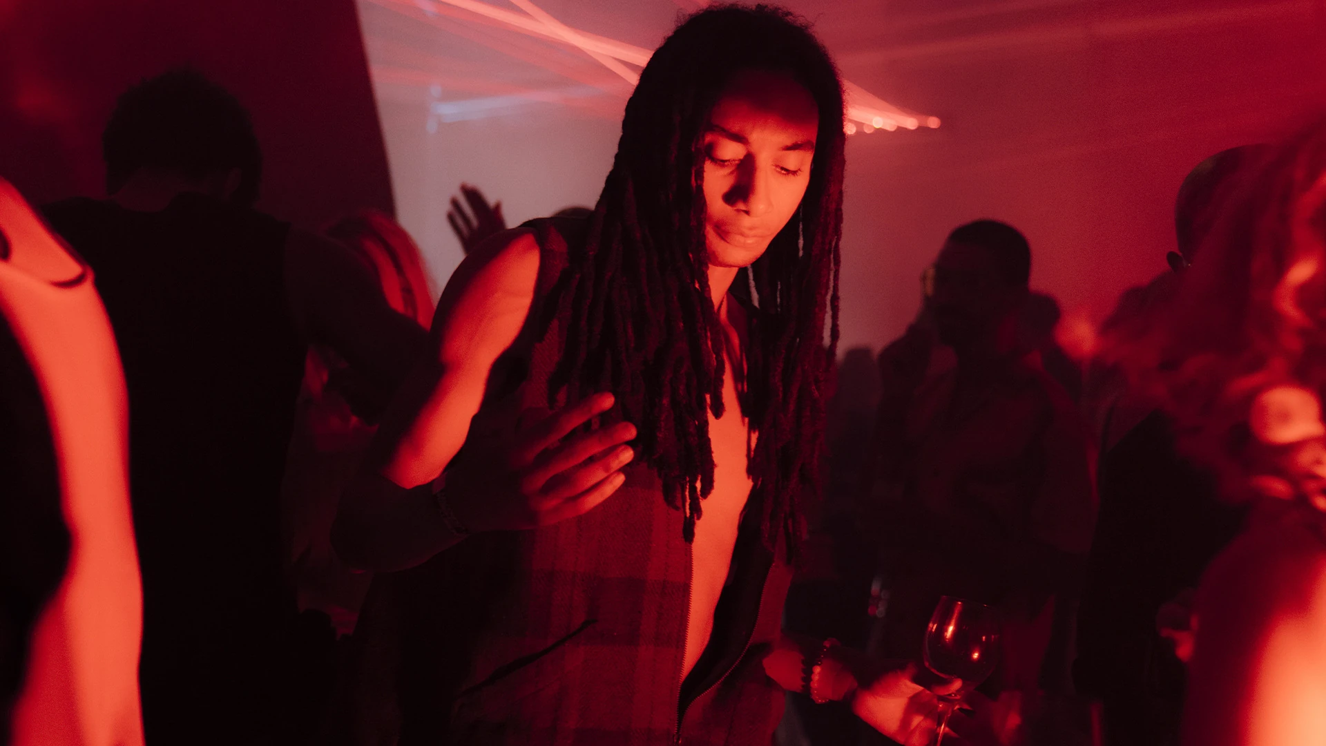 A guest with long locs dancing in the crowd under red light.
